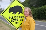 image of woman in yellow work gear in front of sign with a picture of a wombat and slow down warning