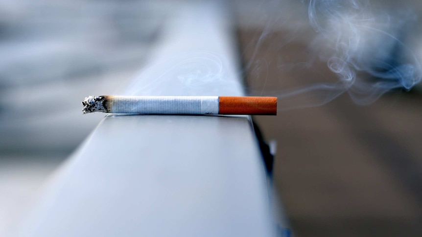 A lit cigarette restomg on a railing