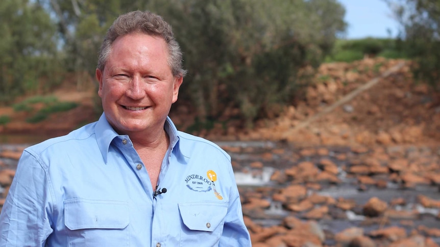 Ginger headed man wearing a blue shirt standing in front of a red rock creek bed lined with gum trees