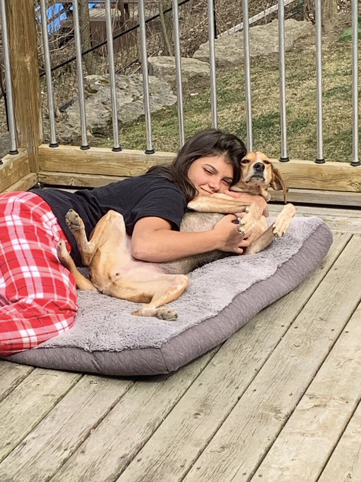 Una mujer joven yace acurrucada en una cama para perros con un perro.