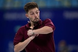 Australian figure skater Brendan Kerry, in a maroon shirt, competing, preparing to spin on his skates