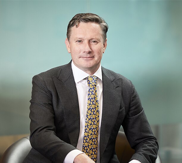 A close up of a middle-aged man in a suit and tie, smiling slightly.