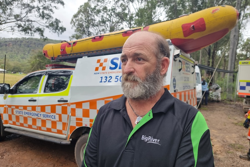 Close up shot of the missing man's dad looking into the distance, standing in front of an SES car.