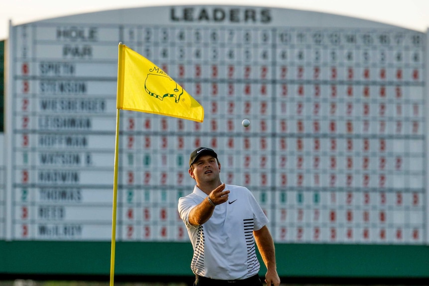 Golfer Patrick Reed catching a ball while the large leaderboard is in the background