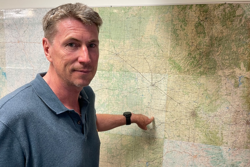 A man stands in front of a map pointing to an affected area 