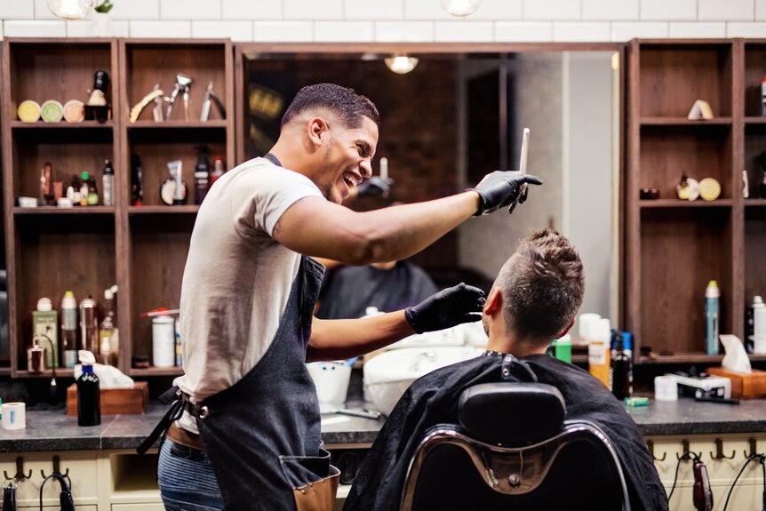 A barber shares a laugh with his client while cutting his hair