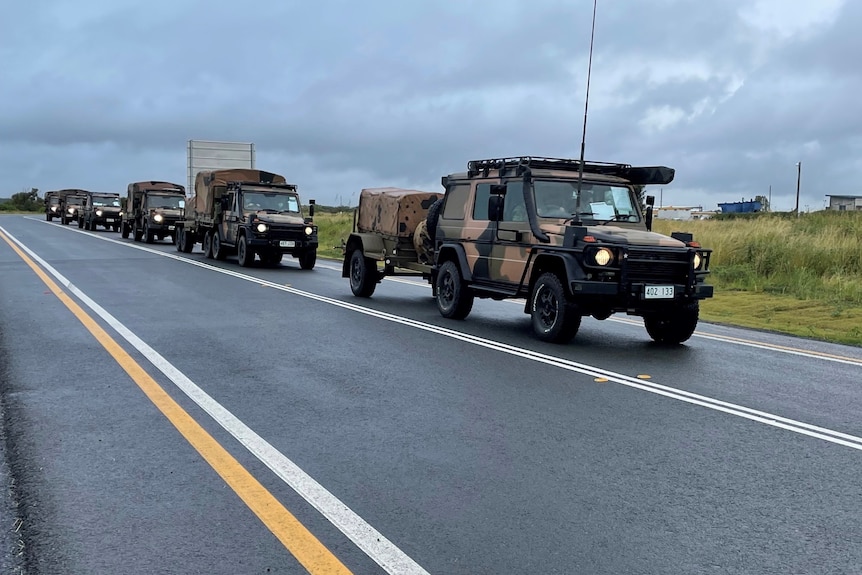 Six military vehicles drive in a convoy while carrying equipment