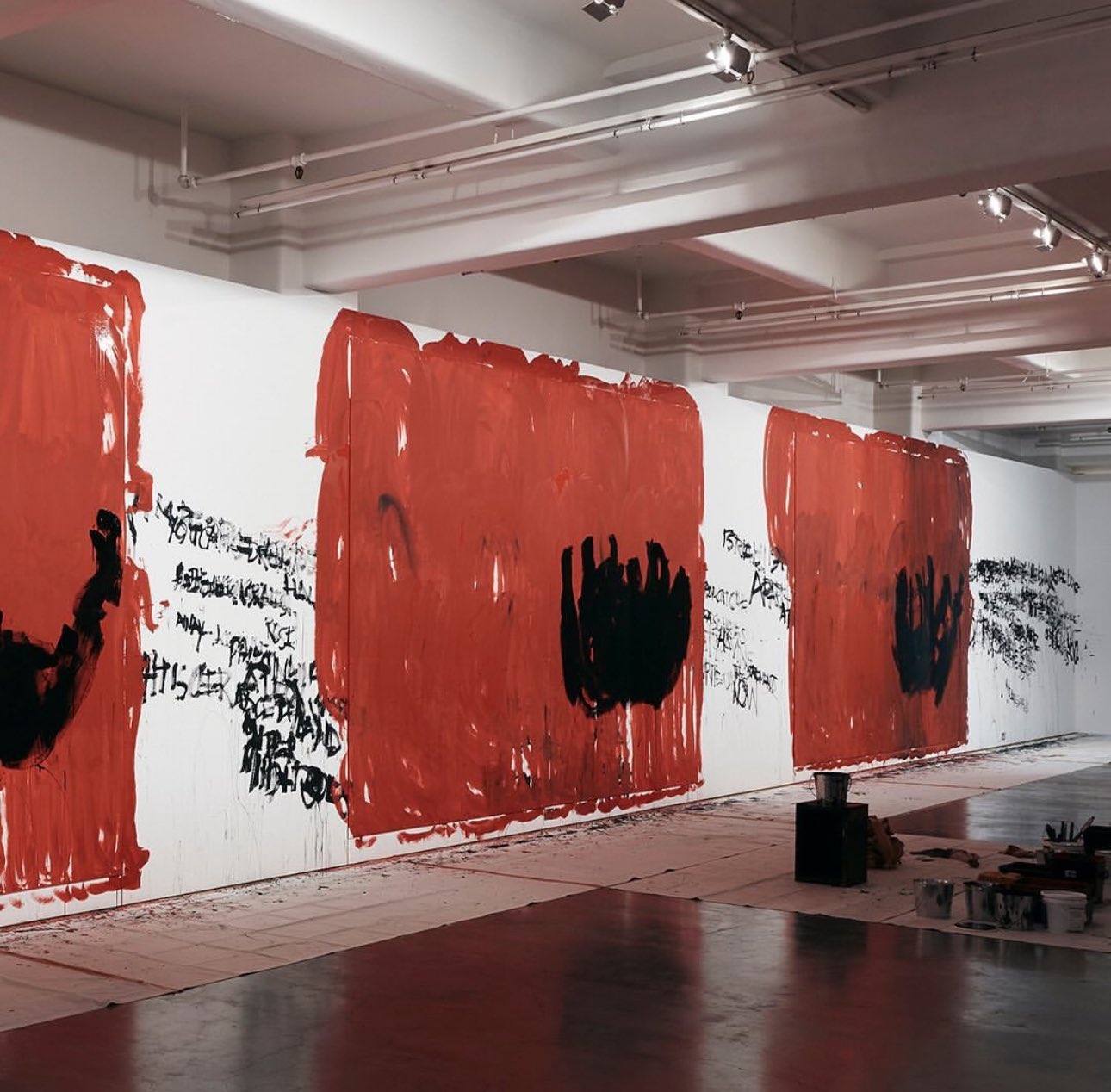 A white gallery wall painted variously with black text and large patches of red and black.