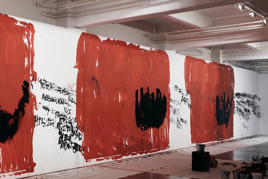 A white gallery wall painted variously with black text and large patches of red and black.