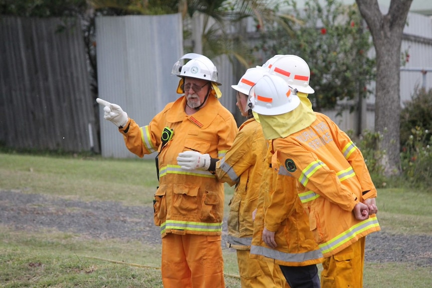 An older man instructs some young people. All are wearing firefighting gear.