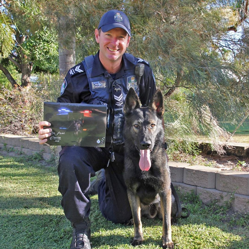 A police officer kneeling beside a police dog and holding a police dog calendar
