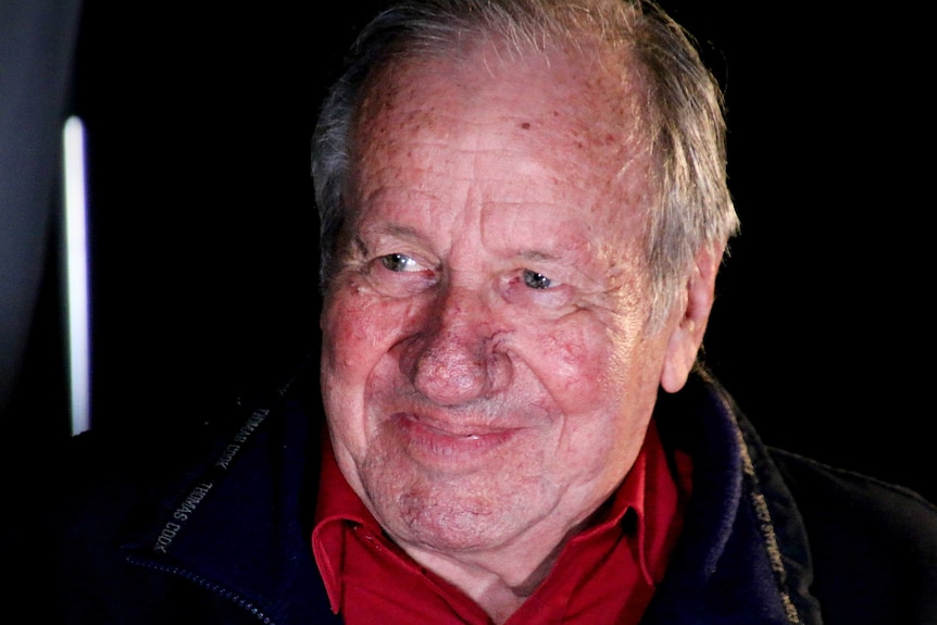 Trevor Mosel smiles posing for a photo against a black backdrop.