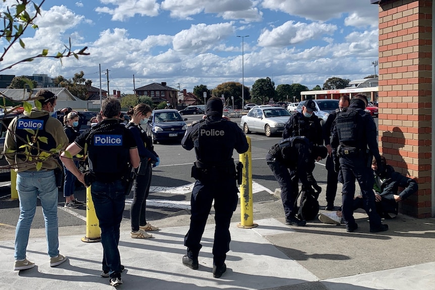 Police detain a man near a car park.