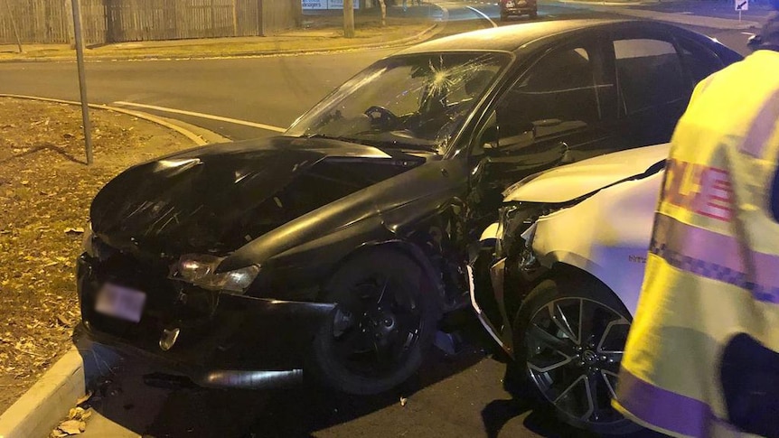 A black sedan with a broken windscreen and dented bonnet crashed at a street corner. A silver car bonnet crushes front door.