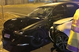 A black sedan with a broken windscreen and dented bonnet crashed at a street corner. A silver car bonnet crushes front door.