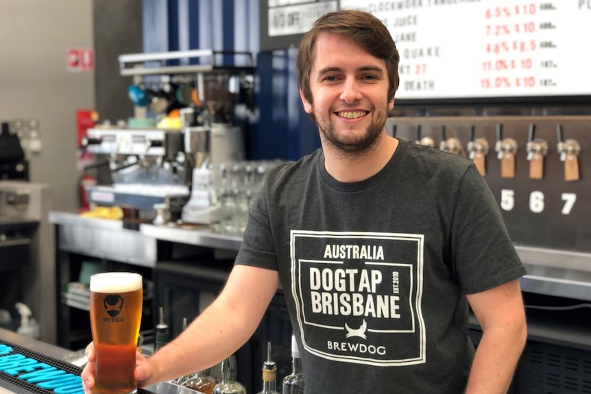 A publican stands at the bar holding a beer