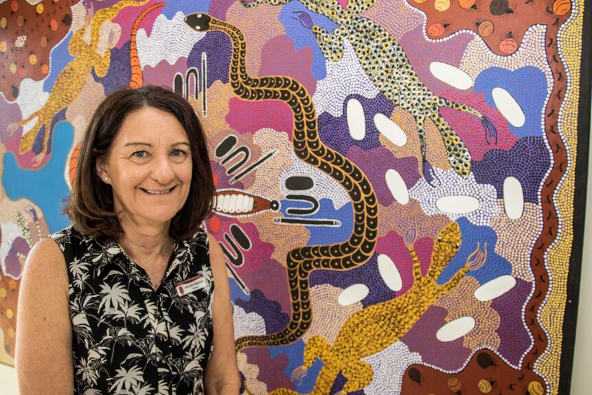 A school teacher in front of an Aboriginal dot painting.