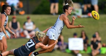 An AFLW player passes the ball in front of her as she is tackled from behind