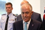 Malcolm Turnbull looks animated while speaking to reporters. He is surrounded by Australian flags.
