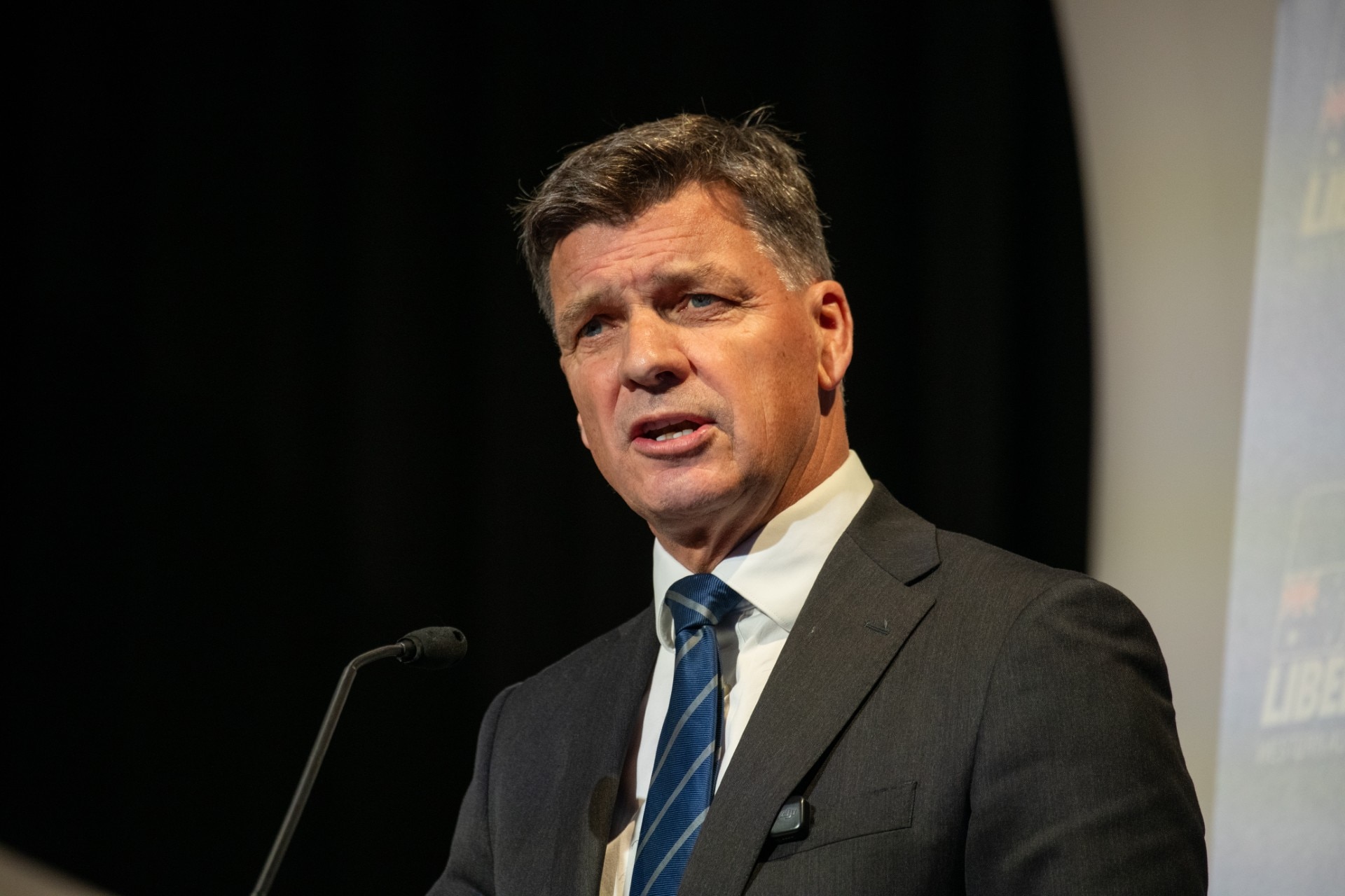 A man with grey hair and in a grey suit speaks with a serious expression