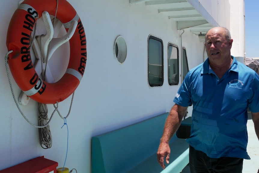 Man in blue shirt walks along the deck of a boat.