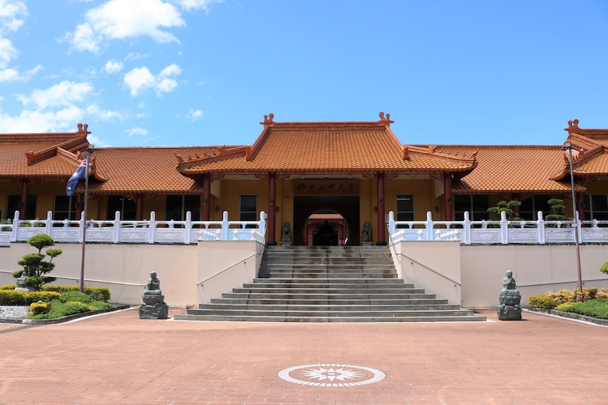 Entrence, quadrangle and steps to a buddhist temple with an Australian flag and manicured gardens.