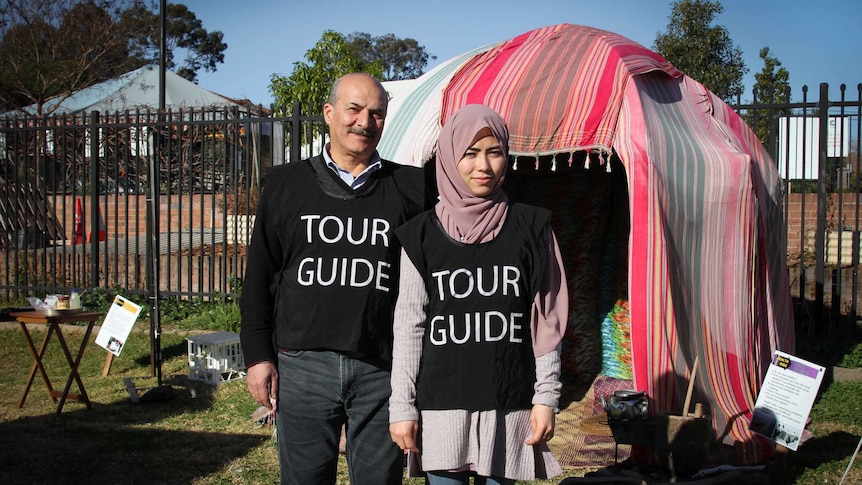 Two people standing out the front of a makeshift tent.