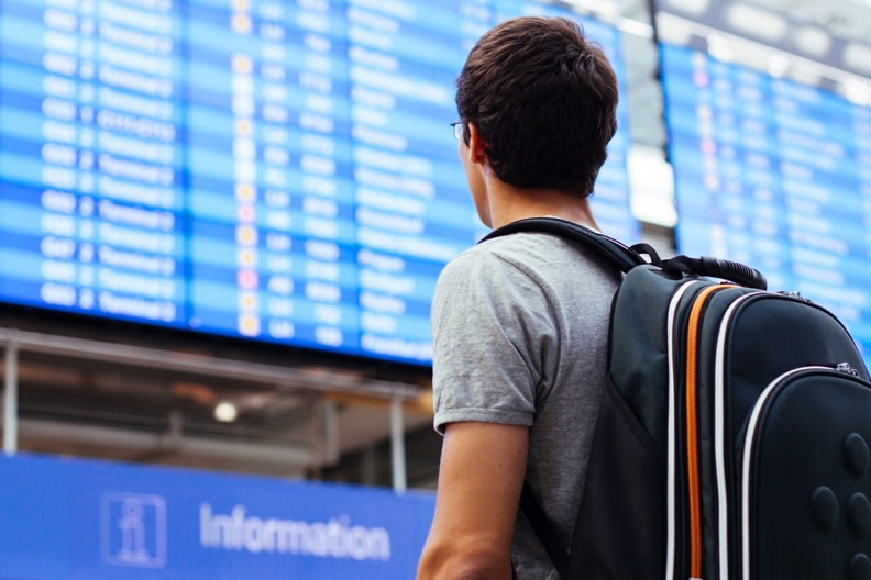Man with backpack looks at airport arrivals board,