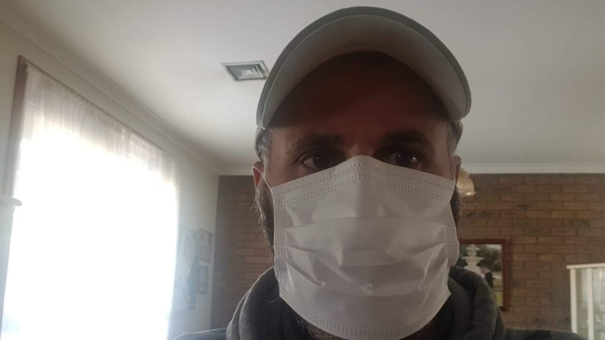 Selfie of Charlie Di Lorenzo wearing a grey hoodie, baseball cap and white surgical mask over his nose and mouth.