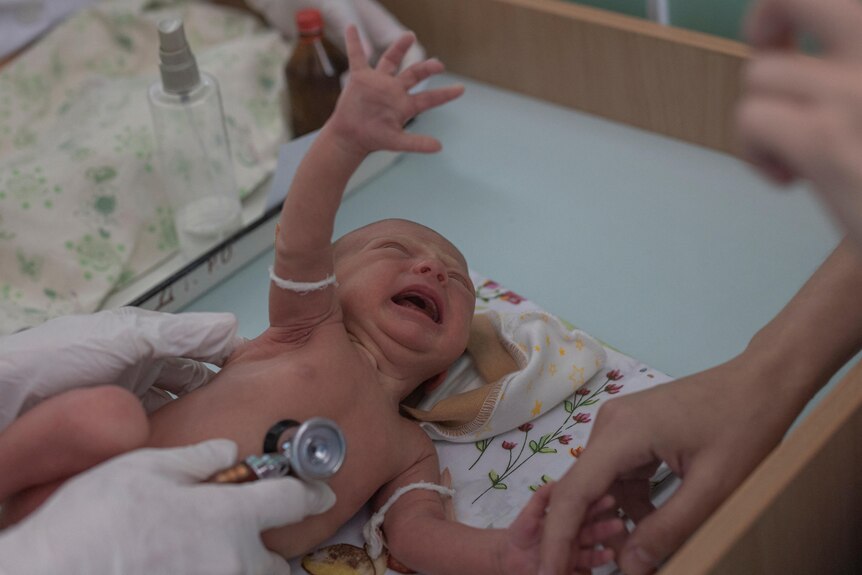 A baby on a hospital bed cried and reached out its hand. 