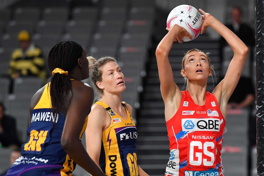 A NSW Swifts Super Netball player holds the ball above her head as she prepares to shoot for goal against the Lightning.