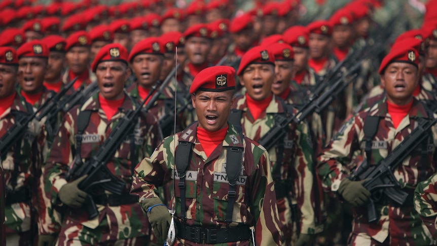 Indonesian special forces soldiers wear red berets and hold assault rifles as they participate in a rally.