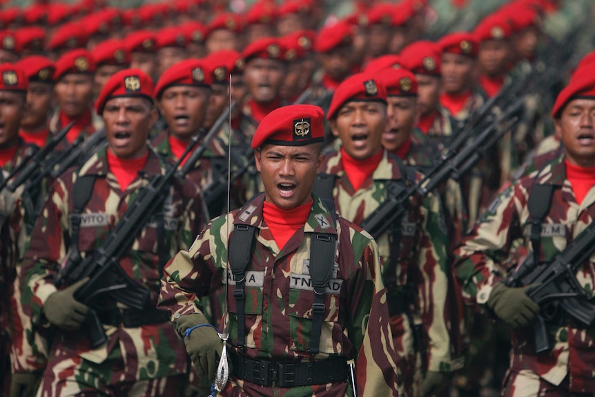Indonesian special forces soldiers wear red berets and hold assault rifles as they participate in a rally.