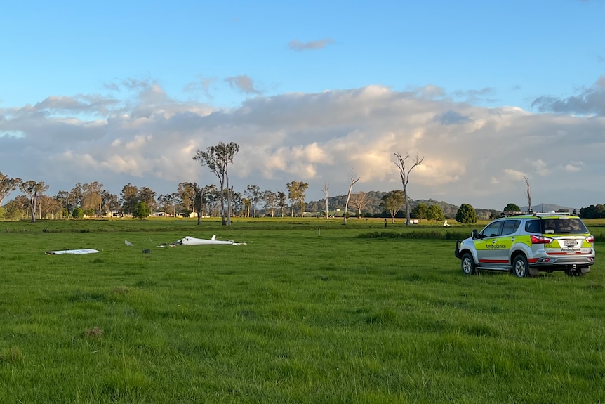 Pieces of a plan in a grassy field near and ambulance.