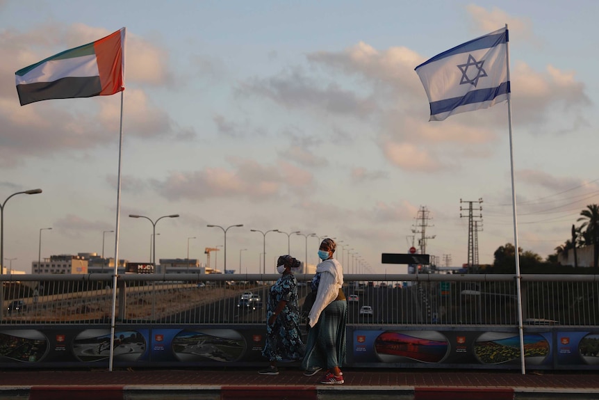 Women wearing face masks against the coronavirus walk past United Arab Emirates and Israeli flags at the Peace Bridge.