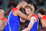 Max Gawn and Clayton Oliver hug as a number of other Melbourne players mull around