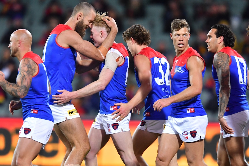 Max Gawn and Clayton Oliver hug as a number of other Melbourne players mull around