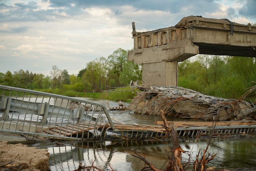 The twisted rubble of a destroyed bridge is seen collapsed into the water. Concrete, metal and wood palings have been torn apart