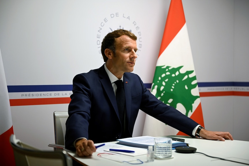 French President Macron sits at a table, looking at the screen of a video conference he has called for donations to Lebanon.