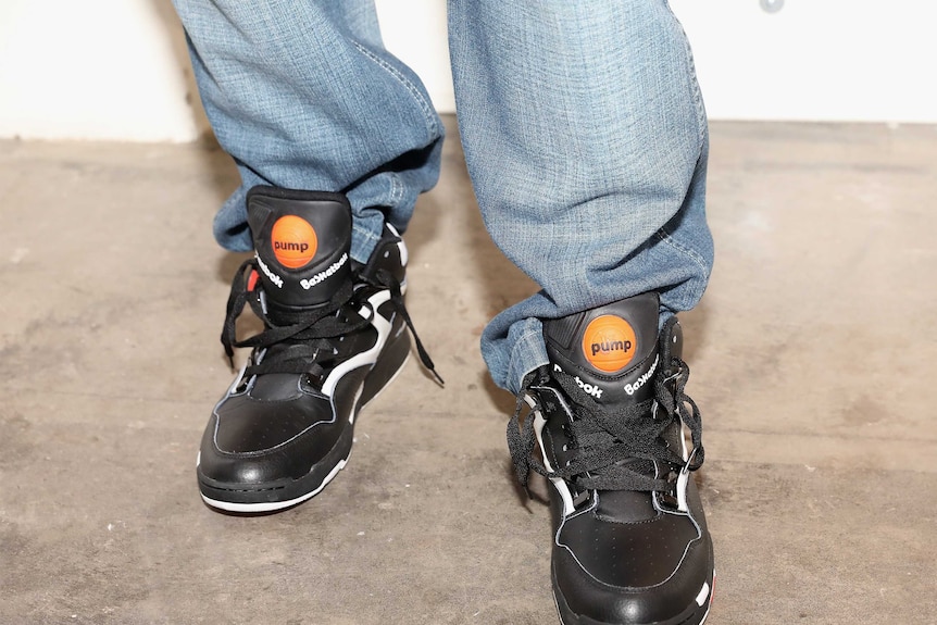 A person wearing baggy blue jeans and a pair of Reebok Pumps.