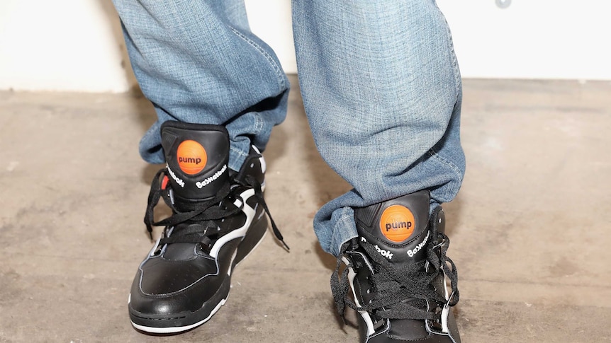 A person wearing baggy blue jeans and a pair of Reebok Pumps.