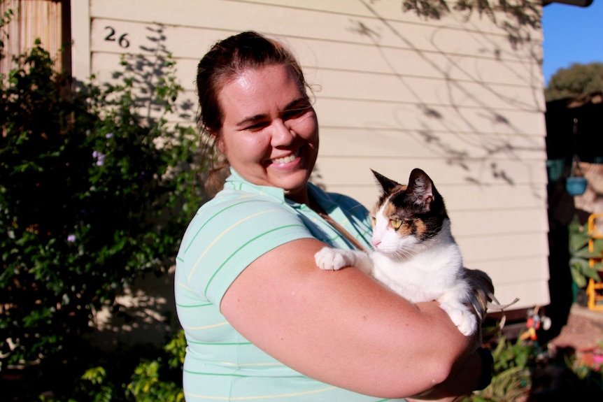 Megan Parkins at home in Longreach  holding a cat in her arms and smiling