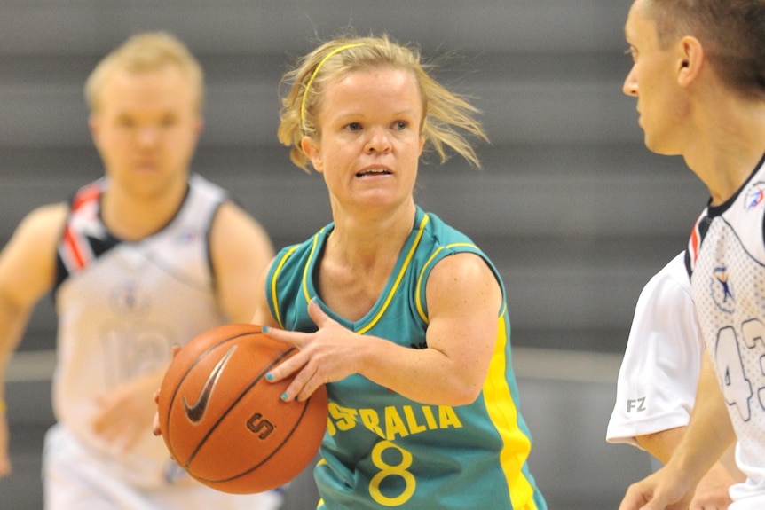 A short statured woman bounces a basketball in an Australia uniform.