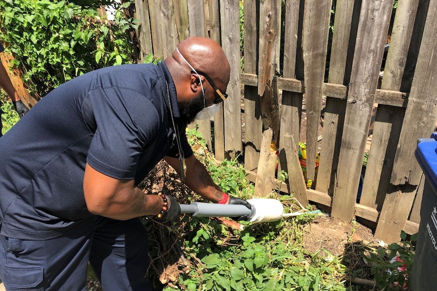 A man is seen applying rodent poison along a fence line.