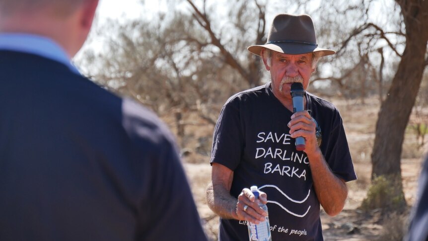 An Aboriginal man wearing a t-shirt reading 'save Darling Barka', talks in to a microphone.