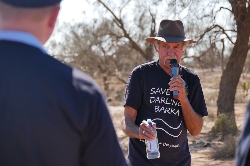 An Aboriginal man wearing a t-shirt reading 'save Darling Barka', talks in to a microphone.