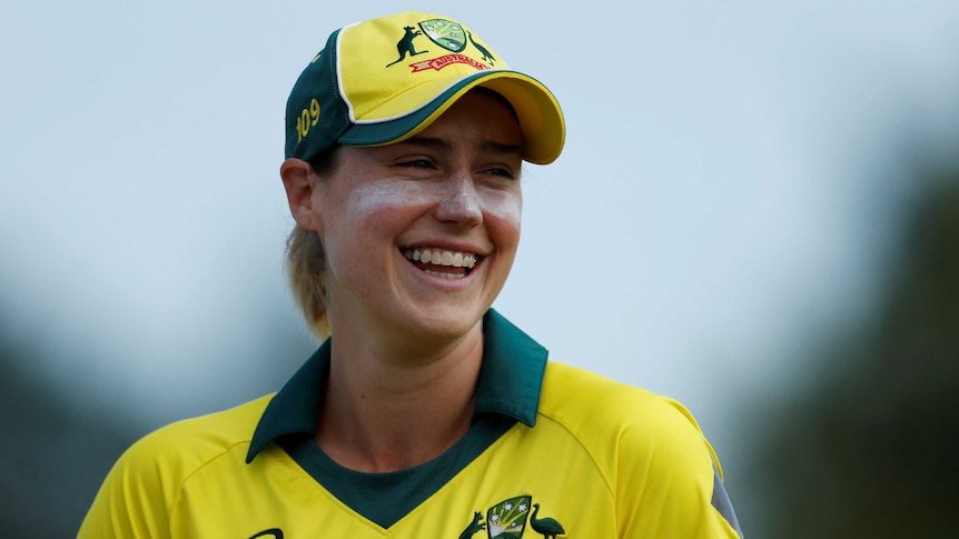 Ellyse Perry smiles, wearing a yellow baseball cap