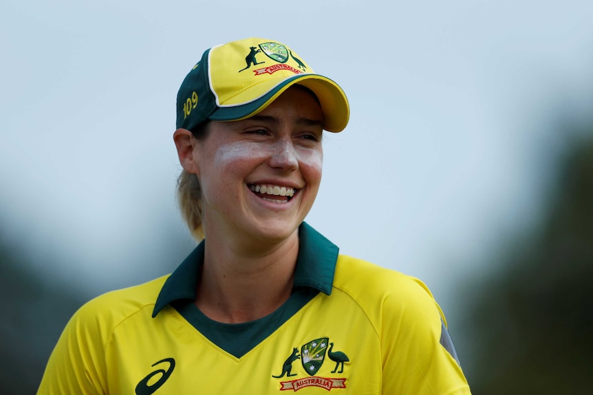 Ellyse Perry smiles, wearing a yellow baseball cap
