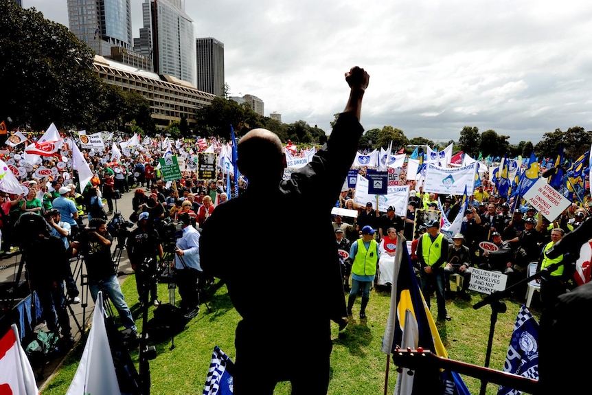 A speaker raises his arm in the air as thousands of trade unionists gaze at the field in Sydney