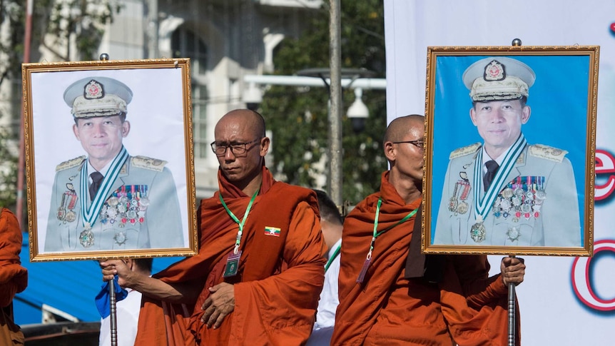 two monks in saffron robes carry large portraits of Myanmar's military commander-in-chief Min Aung Hlaing on stage